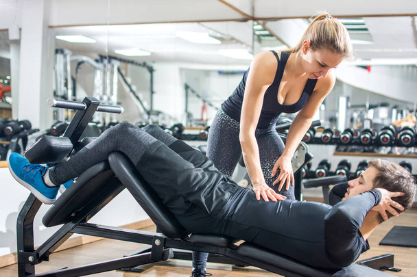 Attraktives Fitness-Girl berührt ihre Freunde Sixpack-Muskeln, während er im Fitnessstudio Sit-Ups auf einem Trainingsgerät macht. - Foto, Bild