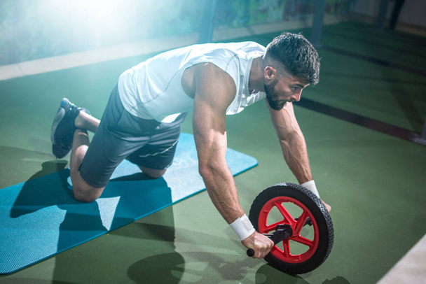 Мускулистый спортсмен тренируется с фитнес-колесом в тренажерном зале. - Фото, изображение