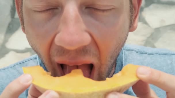 Detailní záběr mladého muže si kousek čerstvého zralého melounového melounu v horkém letním dni venku. Zdravé dietní jídlo na dovolené. Fešák jíst osvěžující chutné ovoce. - Záběry, video