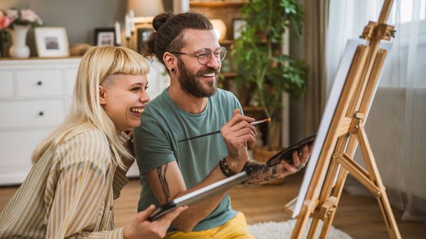 pár festék vászon állvány otthon tartsa ecset segít megtanulni, hogyan kell csinálni festészet tartsa ecset boldog férfi és nő szerelmes barát és barátnő vagy férj és feleség - Fotó, kép
