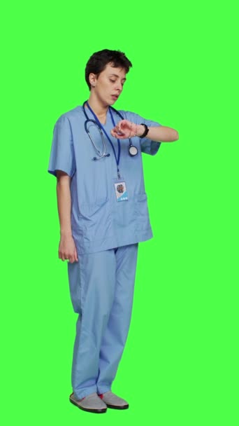 Widok z boku Stresowana pielęgniarka sprawdzająca czas na warcie i czekająca na przyjazd pacjenta na badanie kontrolne, niecierpliwa na zielonym ekranie. Asystent medyczny z peelingiem i stetoskopem - Materiał filmowy, wideo