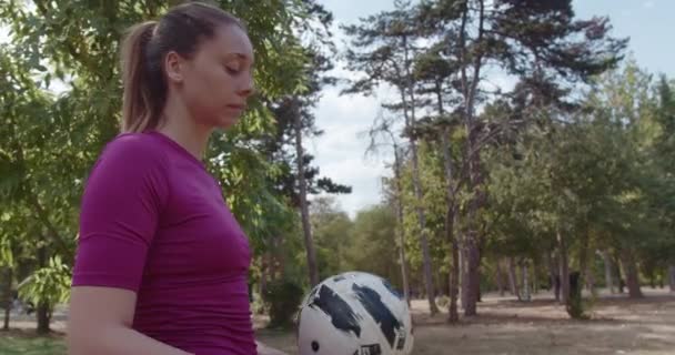 Keskittynyt nuori nainen urheiluvaatteissa tasapainottamassa jalkapalloa sormellaan rehevän puiston rauhallisuudessa. Urheilu-, vapaa-ajan ja jalkapallokoulutuksen käsite. - Materiaali, video