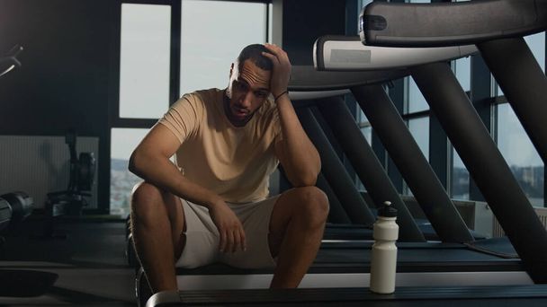 Tired African American man sit on treadmill relax after hard physical workout cardio training in fitness club gym exhausted sweaty sportsman runner thirsty drink water sport bottle healthy lifestyle - Photo, Image