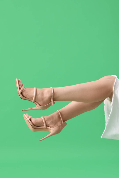 Legs of young woman in stylish beige high heels on green background - Photo, Image