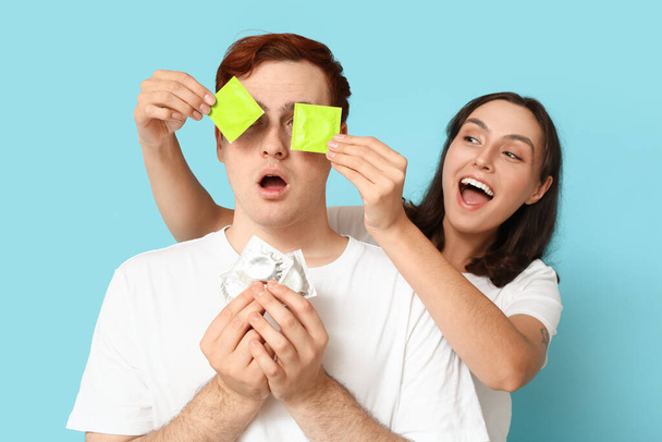 Lustiges junges Paar mit Kondomen auf blauem Hintergrund. Sicheres Sex-Konzept - Foto, Bild