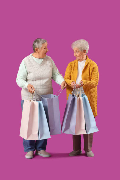 Senior female friends with shopping bags on purple background - Photo, Image