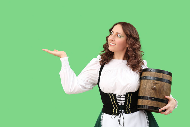 Mujer feliz con barril de cerveza mostrando algo sobre fondo verde. Día de San Patricio - Foto, imagen