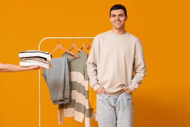 Handsome young happy man and rack with stylish clothes on yellow background - Photo, Image