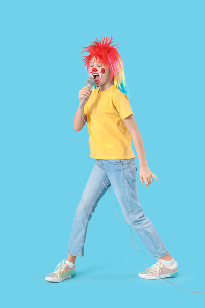 Zabawna dziewczyna w kostiumie klauna z mikrofonem na niebieskim tle. Święto prima aprilis - Zdjęcie, obraz