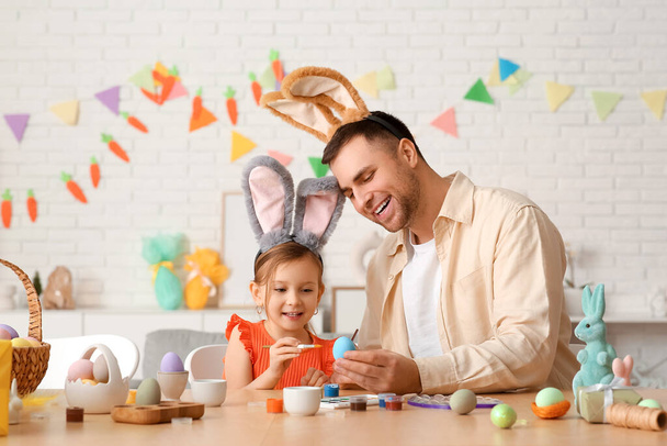 klein meisje met haar vader in konijnenoren schilderen paaseieren thuis - Foto, afbeelding
