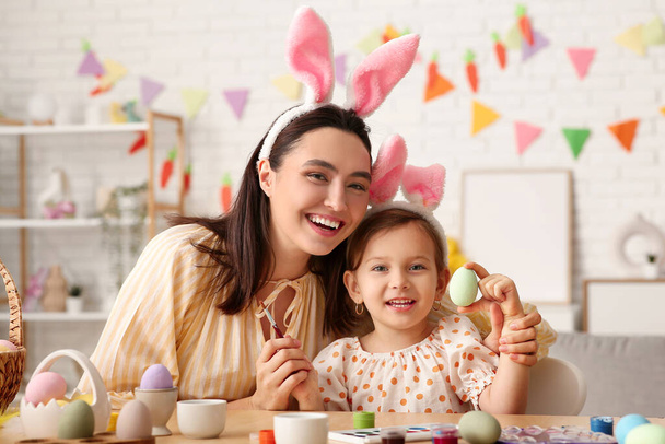 Petite fille avec sa mère dans des oreilles de lapin peignant des œufs de Pâques à la maison - Photo, image
