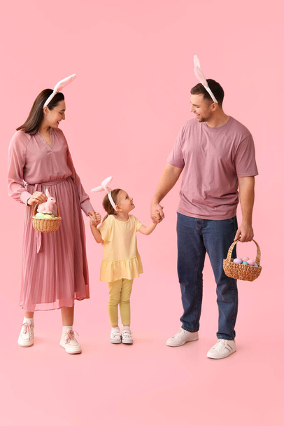 Happy family in bunny ears holding baskets with Easter eggs on pink background - Photo, Image