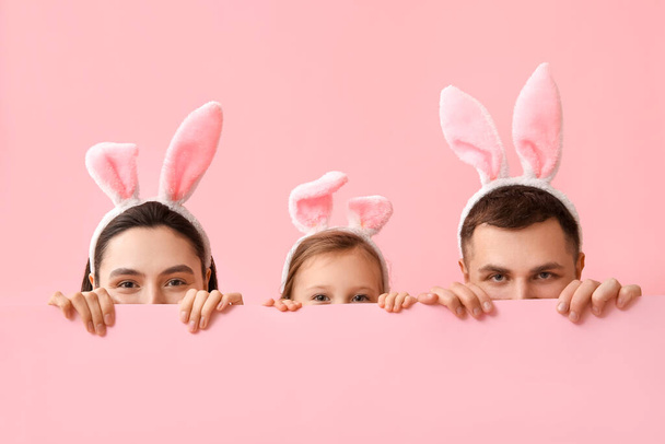 Szczęśliwa rodzina w uszach króliczka wielkanocnego ukrywa się na różowym tle - Zdjęcie, obraz
