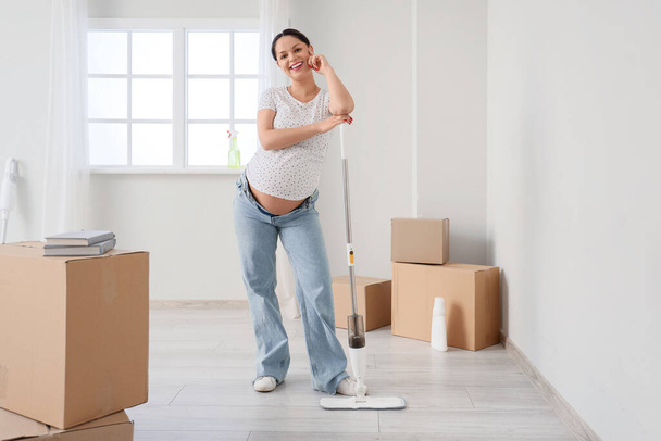 Mujer embarazada joven con fregona de piso en nuevo apartamento - Foto, Imagen
