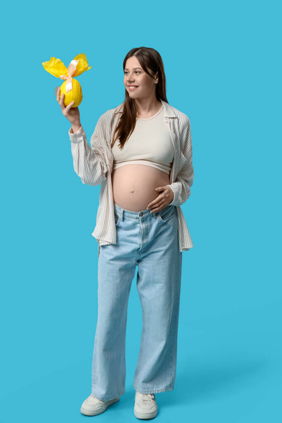 Hermosa joven embarazada con huevo de regalo de Pascua sobre fondo azul - Foto, Imagen