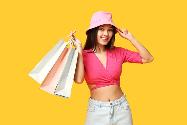 Mulher asiática jovem na moda em roupas elegantes com sacos de compras no fundo amarelo - Foto, Imagem