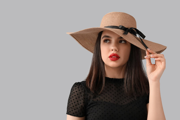 Hermosa joven con sombrero y labios rojos sobre fondo gris - Foto, Imagen
