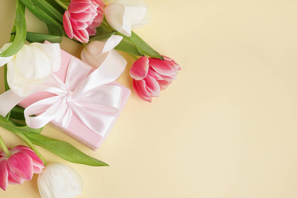 Caja de regalo y hermosos tulipanes sobre fondo amarillo - Foto, imagen