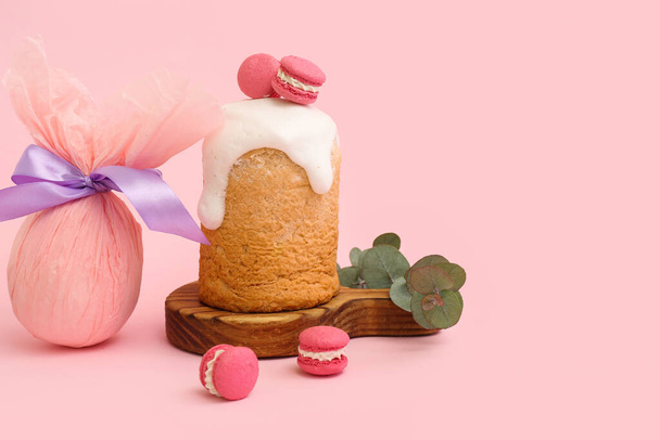 Drewniana deska z tortem wielkanocnym, słodkimi makaronami i jajkiem upominkowym na różowym tle - Zdjęcie, obraz