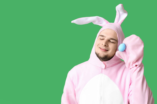 Yeşil arka planda Paskalya yumurtası olan tavşan kostümlü genç adam. - Fotoğraf, Görsel
