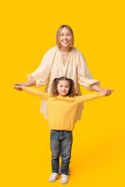 Мама играет со своим ребенком на жёлтом фоне. День матери - Фото, изображение