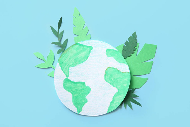 Papier planète Terre avec des feuilles vertes sur fond bleu. Fête de la Terre. - Photo, image
