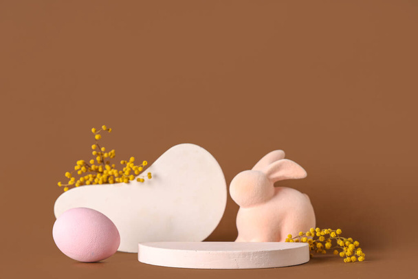 Pódiums decorativos con huevo de Pascua, conejito de juguete y flores mimosas sobre fondo marrón - Foto, imagen