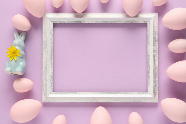 Beautiful composition with frame, painted Easter eggs and bunnies on lilac background - Photo, Image