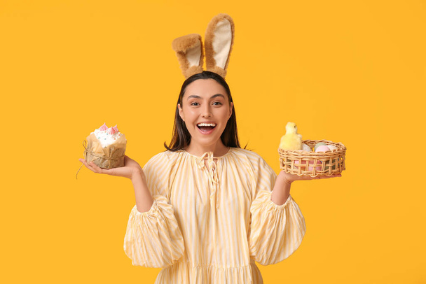 Красива молода жінка в вухах кролика з солодким пирогом, яйцями і куркою на жовтому фоні - Фото, зображення
