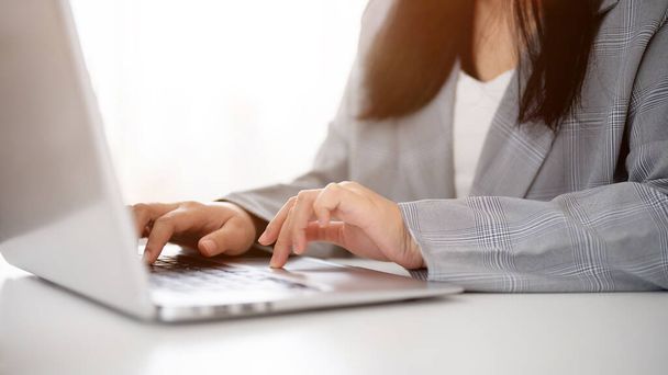 Oříznutý obraz podnikatelky pracující nebo procházející notebook, jak píše na klávesnici notebooku a pracuje v moderní světlé kanceláři. - Fotografie, Obrázek