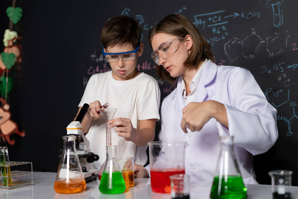 Öğretmen, laboratuarda öğrenciyi destekliyor. Öğrenci ve öğretmen cam kapta sıvı kullanarak STEM sınıfında kimya bilimi üzerine deney yapıyorlar. Karıştırma çözeltisi. Etkinlik. - Fotoğraf, Görsel