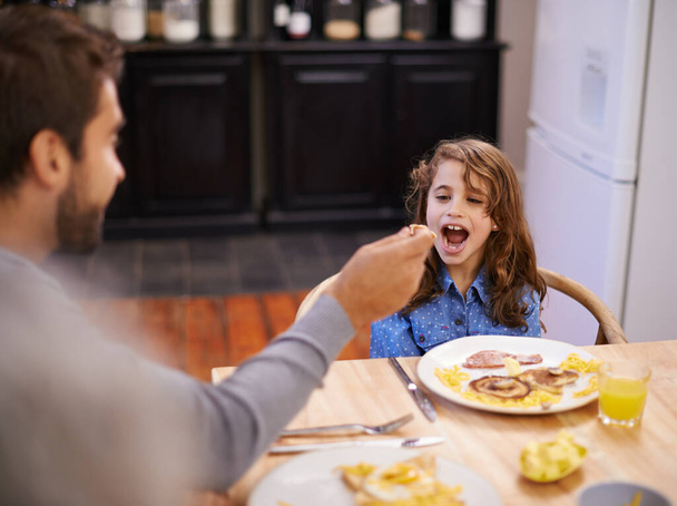 Isä, ruokinta ja tyttö syövät aamiaista kotona keittiössä terveyden, ravitsemuksen ja hyvinvoinnin vuoksi. Lapsi, isä ja onnellinen ruoka omakotitalossa yhdessä aamuaterian, kehityksen ja ruokavalion vuoksi. - Valokuva, kuva