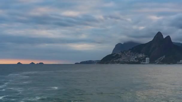 Atemberaubender Zeitraffer einer Küstenszene mit Meer, Bergen und Favela unter einem traumhaften Sonnenuntergang, der viel Textfläche bietet. - Filmmaterial, Video