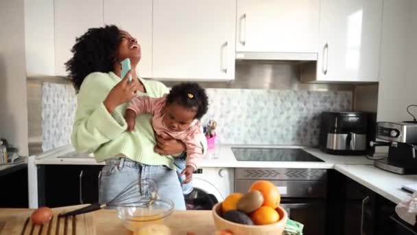 Umtriebige junge Mutter kocht, während sie ihr neugieriges Kleinkind hält, Multitasking zu Hause. - Filmmaterial, Video