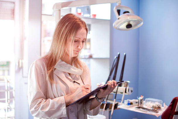 Naispuolinen hammaslääkäri kirjoittaa leikepöydälle hammaslääkärin toimistossa - Valokuva, kuva