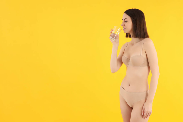 Chica delgada en ropa interior bebe agua de un vaso. - Foto, imagen