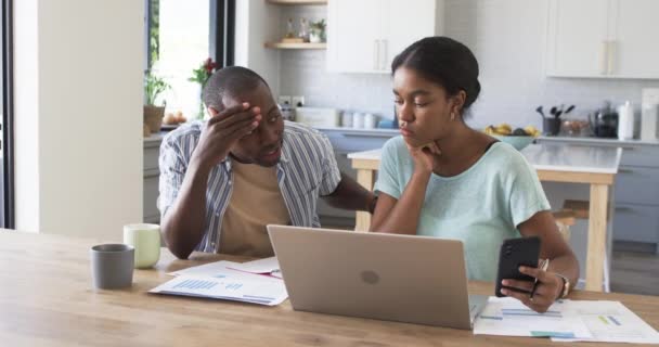 A young African American couple is managing finances at home using a laptop. The husband looks stressed while the wife holds a smartphone, surrounded by bills, unaltered, slow motion - Séquence, vidéo