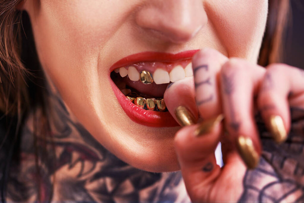 Woman, bite and hand with tattoo and nails for grill on tooth and ink design for creative and unique. Art on skin for bold and cool for statement and funky for trend, gold and pattern with red lips. - Фото, изображение