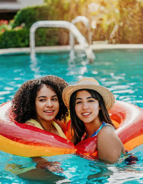 view of two young middle aged  women, relaxing in a pool floatie together in summer time and look at camera with complicity. girlfriends. couple lgbtq concept - Photo, Image