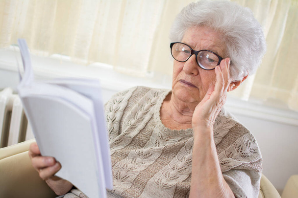 Mujer mayor concentrada leyendo libro en casa. - Foto, Imagen