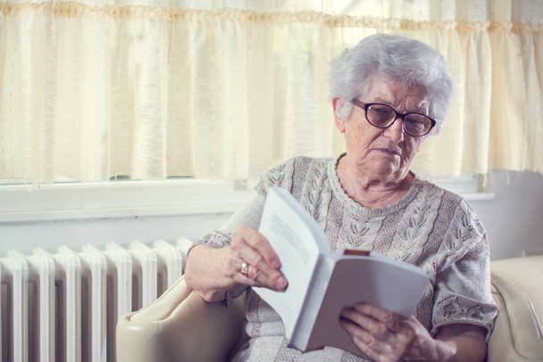 Retrato de mujer mayor leyendo libro en casa. - Foto, Imagen