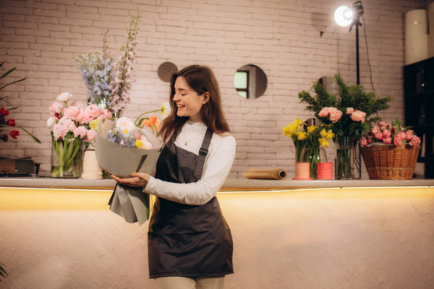 Привлекательная женщина, владелица цветочного магазина в фартуке, держит букет цветов в цветочном магазине. Высокое качество фото - Фото, изображение