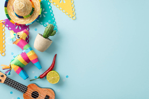 Cinco de Mayo dekorasyonlarının üst görüntüsü: şapka, bir vihuela, tencerede kaktüs, renkli bir pinata, bayrak çelengi, kırmızı biber, konfeti, pastel mavisi bir sahneye yerleştirilmiş, metin için yer - Fotoğraf, Görsel
