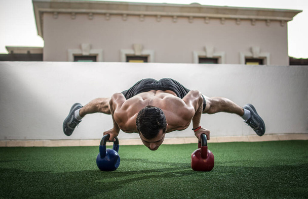 Muscular shirtless man doing handstand on kettlebells. - Photo, Image