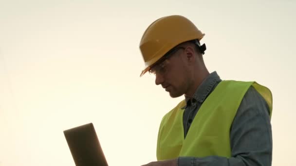 Retrato del auditor de energía que trabaja en un ordenador portátil mientras está de pie cerca de un pilón eléctrico. Movimiento lento - Metraje, vídeo