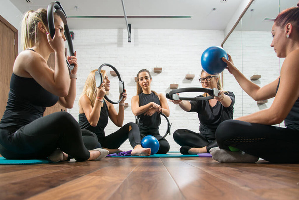 Happy sporty girls having fun in gym. Girlfriends throwing fitness ball through pilates ring in health club. - Foto, immagini
