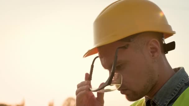 Sıkı şapkalı inşaat işçisinin yakın plan portresi. Güvenlik gözlüklerini takıyor, gülümsüyor ve mesafeye bakıyor. Yavaş çekim - Video, Çekim