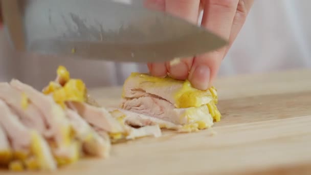 De chef gebruikt een scherp mes om de gekookte kippenborst in blokjes te snijden. Houten bord, groenten op achtergrond, macro, zijaanzicht - Video