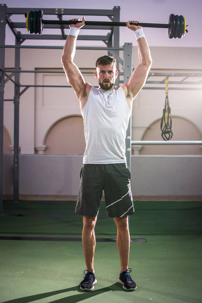 Портрет м'язистого чоловіка, який виконує вправи з барбелом у спортивному залі на відкритому повітрі. - Фото, зображення