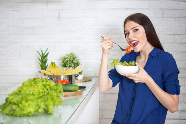 Mujer joven comiendo ensalada mixta en la cocina - Foto, Imagen